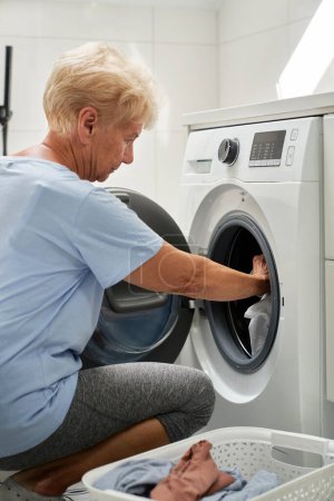 Téléchargez les photos : Femme âgée chargeant une machine à laver - en image libre de droit