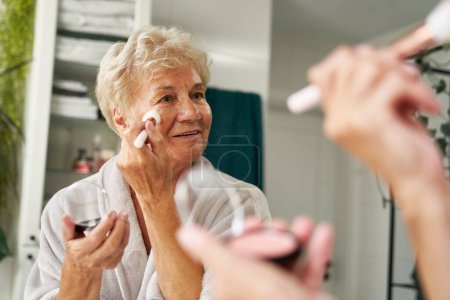 Téléchargez les photos : Femme âgée faisant maquillage dans la salle de bain - en image libre de droit