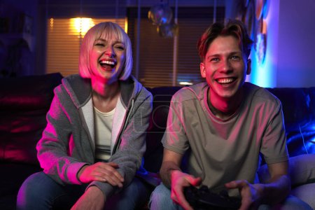Foto de Joven pareja caucásica jugando videojuegos con almohadillas de juego mientras está sentado en el sofá - Imagen libre de derechos