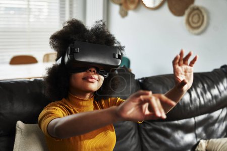 Téléchargez les photos : Adolescente portant un simulateur de réalité virtuelle pour jouer au jeu vidéo dans le salon - en image libre de droit
