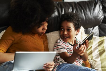 Téléchargez les photos : Plan large de deux enfants naviguant sur la tablette numérique dans le salon - en image libre de droit