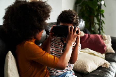 Photo for Siblings wearing virtual reality simulator to play video game in the living room - Royalty Free Image