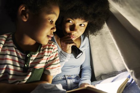 Téléchargez les photos : Deux enfants naviguant tablette numérique sous couverture la nuit - en image libre de droit
