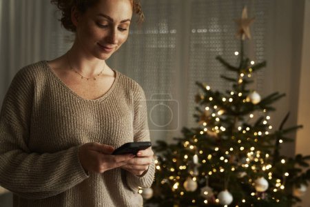 Téléchargez les photos : Jeune femme caucasienne utilisant le téléphone la nuit pendant Noël - en image libre de droit