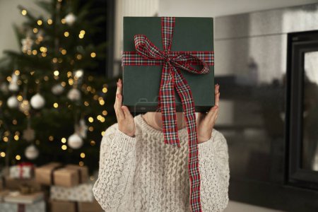 Téléchargez les photos : Femme méconnaissable se cachant face derrière une boîte cadeau de Noël - en image libre de droit