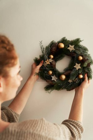 Téléchargez les photos : Femme accrochant une couronne de Noël sur le mur - en image libre de droit