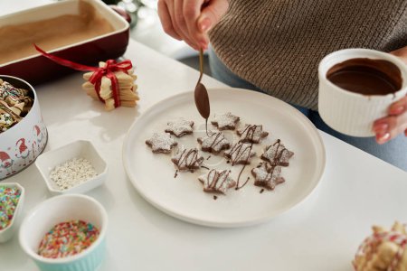 Photo for Unrecognizable woman decorating Christmas cookies with a chocolate glaze - Royalty Free Image