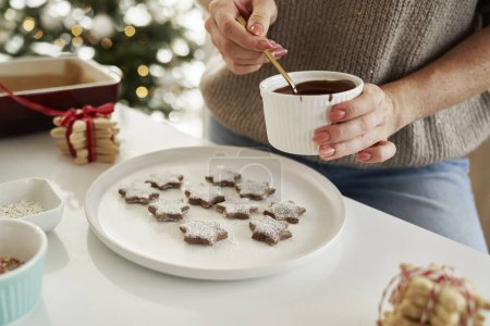 Foto de Mujer irreconocible decorando galletas de Navidad con un glaseado de chocolate - Imagen libre de derechos