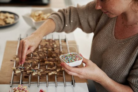 Photo for Caucasian woman decorating Christmas cookies with sugar sprinkles - Royalty Free Image