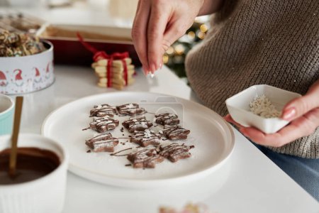 Foto de Mujer caucásica decorando galletas de Navidad con chispas de azúcar blanco - Imagen libre de derechos