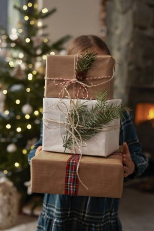 Téléchargez les photos : Enfant méconnaissable portant une pile de cadeaux de Noël - en image libre de droit