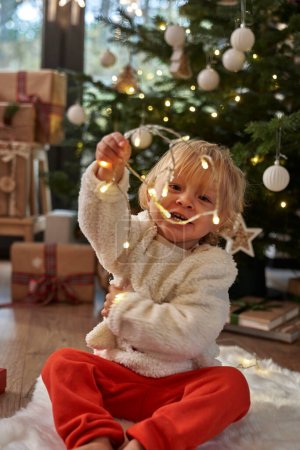 Foto de Niño sentado en el suelo y jugando con luces de Navidad - Imagen libre de derechos