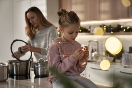 Photo for Caucasian girl playing with Christmas lights in the kitchen - Royalty Free Image