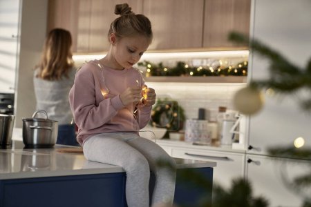Photo for Caucasian girl playing with Christmas lights in the kitchen - Royalty Free Image