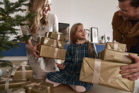 Téléchargez les photos : Famille joyeuse de trois partageant des cadeaux de Noël à côté de l'arbre de Noël - en image libre de droit
