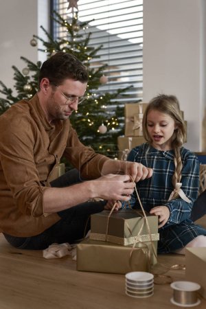 Téléchargez les photos : Père et fille emballer cadeaux de Noël à côté de l'arbre de Noël - en image libre de droit