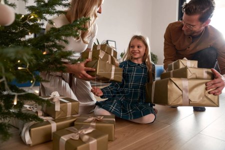 Photo for Cheerful parents sharing Christmas presents with their daughter - Royalty Free Image