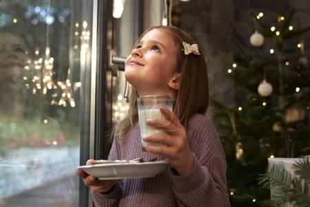 Photo for Little girl looking through the window and waiting for Santa Claus - Royalty Free Image
