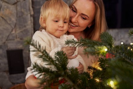 Foto de Madre llevando a un niño pequeño y de pie junto al árbol de Navidad - Imagen libre de derechos