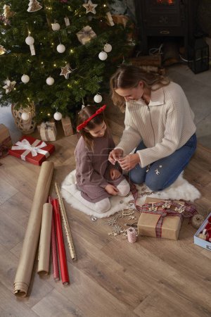 Téléchargez les photos : Vue grand angle de la fille caucasienne et de la mère enveloppant les cadeaux de Noël sur le sol - en image libre de droit