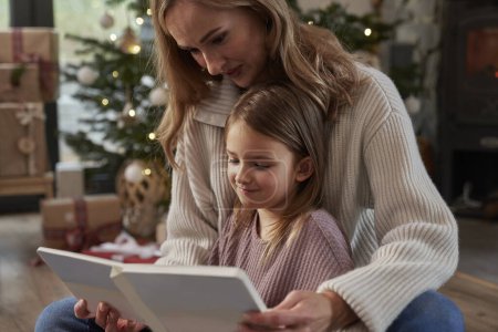 Téléchargez les photos : Mère et fille lisant le livre pendant la période de Noël - en image libre de droit