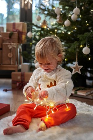 Foto de Niño sentado en el suelo y jugando con luces de Navidad - Imagen libre de derechos