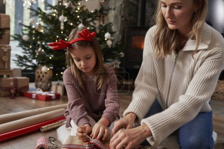 Téléchargez les photos : Focus fille et mère enveloppant cadeaux de Noël sur le sol - en image libre de droit