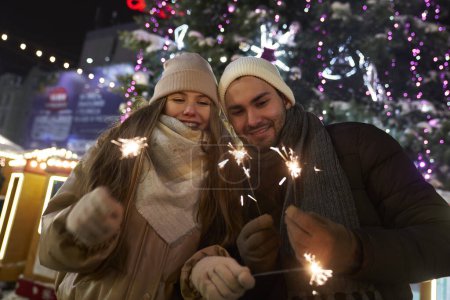 Téléchargez les photos : Couple caucasien avec des étincelles pendant la fête du Nouvel An en plein air - en image libre de droit