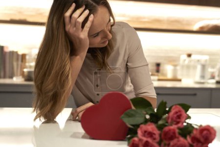 Photo for Sad woman looking at box of chocolates and bunch of roses - Royalty Free Image