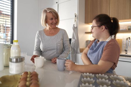 Foto de Síndrome de Down mujer y su madre charlando en la cocina - Imagen libre de derechos