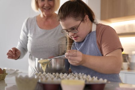 Foto de Síndrome de Down mujer y su madre haciendo cupcakes caseros - Imagen libre de derechos