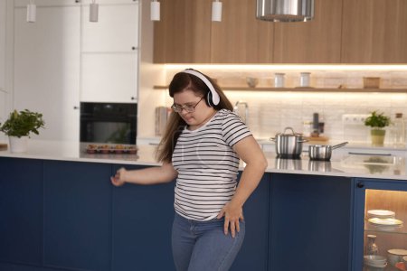 Foto de Síndrome de Down mujer usando auriculares y bailando en la sala de estar - Imagen libre de derechos