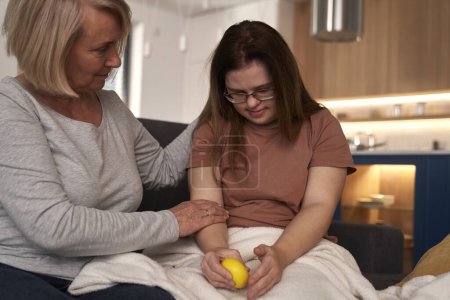 Photo for Stressed down syndrome woman sitting on sofa and talking to her mother - Royalty Free Image