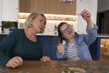 Téléchargez les photos : Joyeuse femme du syndrome du duvet et sa mère assemblant des puzzles à la maison - en image libre de droit