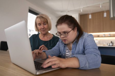 Téléchargez les photos : Femme trisomique utilisant l'ordinateur avec l'aide de sa mère - en image libre de droit