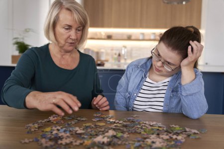Photo for Focus down syndrome woman and her mother assembling puzzles at home - Royalty Free Image