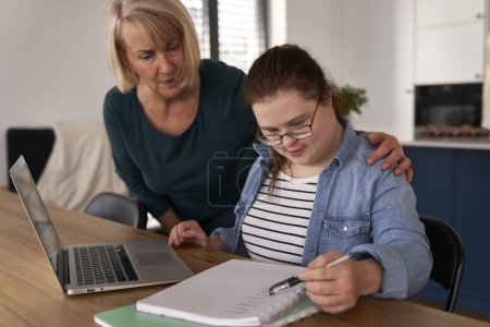 Foto de Síndrome de Down mujer que estudia en el ordenador y portátil con la ayuda de su madre - Imagen libre de derechos