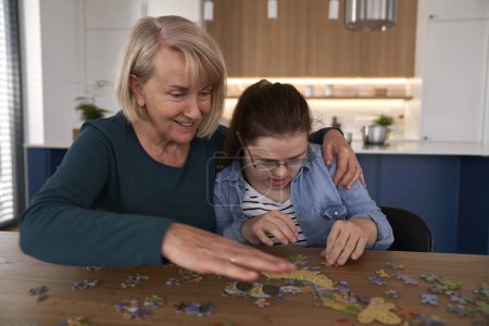 Photo for Joyful down syndrome woman and her mother assembling puzzles at home - Royalty Free Image