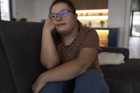 Téléchargez les photos : Thoughtful down syndrome femme assise dans le salon et regardant loin - en image libre de droit