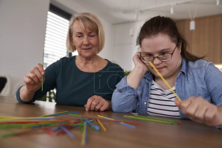 Foto de Síndrome de Down mujer y su madre jugando recoger palos en casa - Imagen libre de derechos