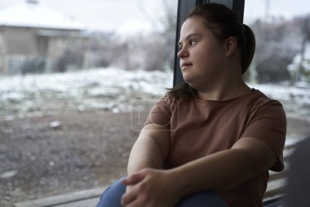 Téléchargez les photos : Femme de syndrome pensif vers le bas assis à côté de la fenêtre et regardant loin - en image libre de droit
