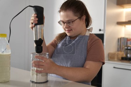 Téléchargez les photos : Down femme trisomique cuisson dans la cuisine domestique - en image libre de droit
