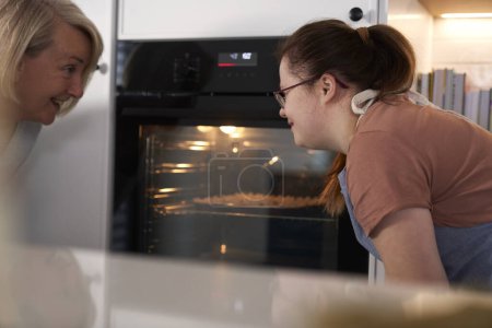 Foto de Síndrome de Down mujer y su madre esperando cupcakes caseros en el horno - Imagen libre de derechos