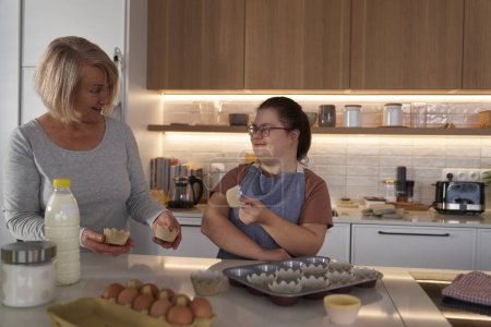 Téléchargez les photos : Femme trisomique et mère préparant des cupcakes maison - en image libre de droit