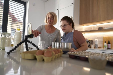 Photo for Down syndrome woman and her mother using recipe on the phone - Royalty Free Image