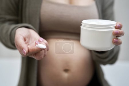 Foto de Mujer embarazada sosteniendo una crema hidratante - Imagen libre de derechos