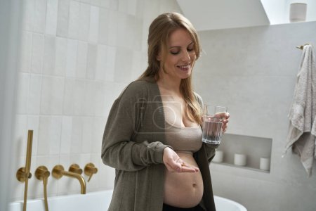 Téléchargez les photos : Femme enceinte caucasienne tenant des suppléments nutritionnels et un verre d'eau - en image libre de droit