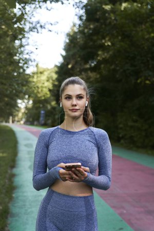 Foto de Mujer en ropa deportiva en la pista sosteniendo un teléfono móvil - Imagen libre de derechos