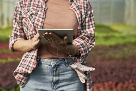 Foto de Mujer botánica caucásica parada en el invernadero y usando tableta digital - Imagen libre de derechos