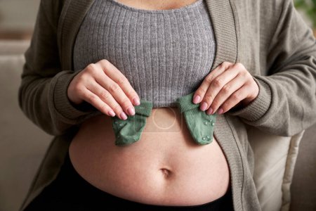 Foto de Mujer embarazada irreconocible sosteniendo calcetines de bebé en su estómago - Imagen libre de derechos